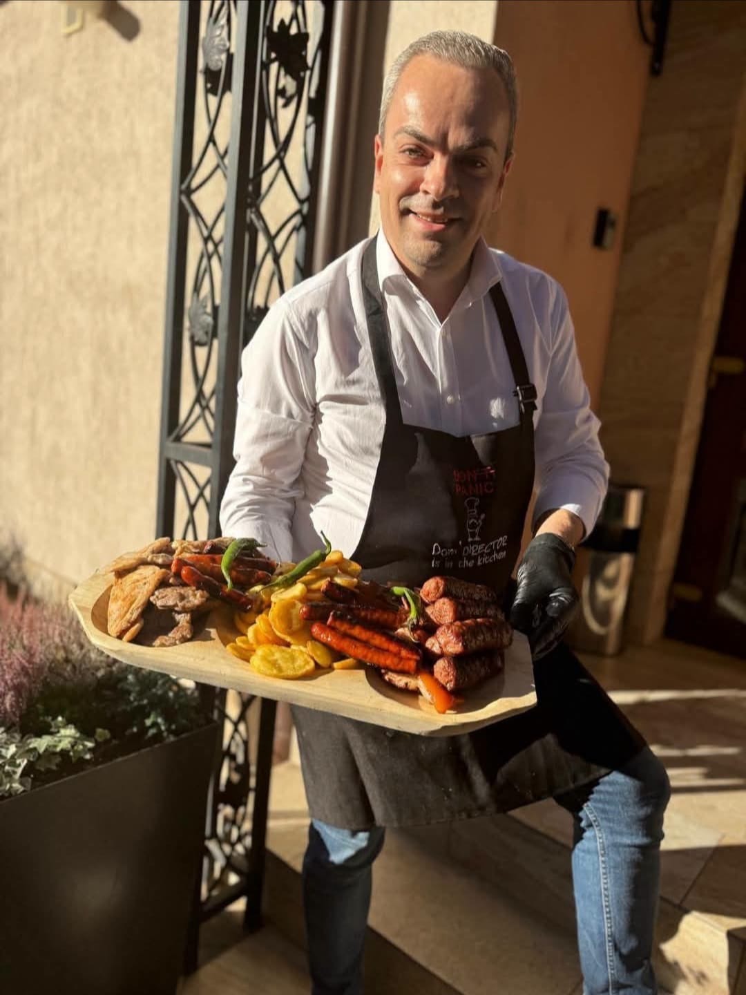 Gazda restaurantului CREMA, cu un platou de lemn plin cu mici, cârnăciori, grătar și cartofi