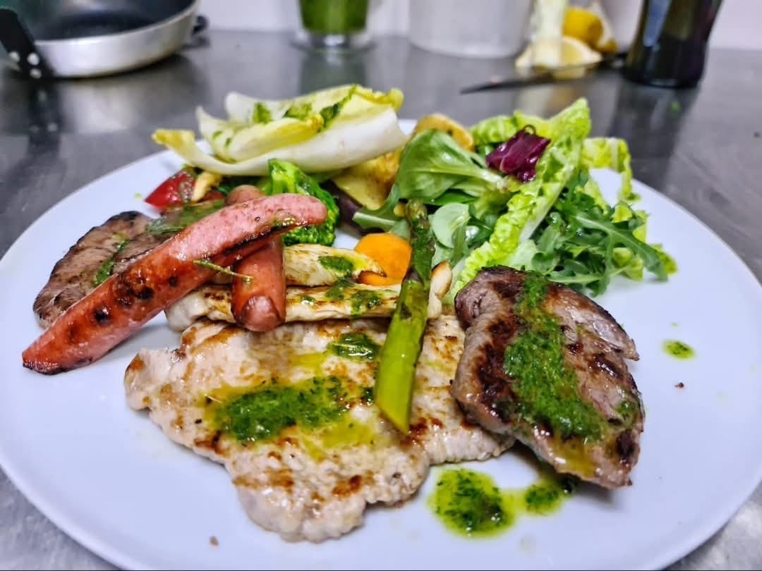 Platou cu preparate la grătar, cârnăciori, legume și salată verde, cu sos de ierburi