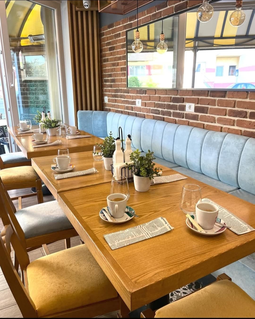 Sala restaurantului CREMA: canapea albastră lângă zidul de cărămidă, mese de lemn pregătite cu cafea