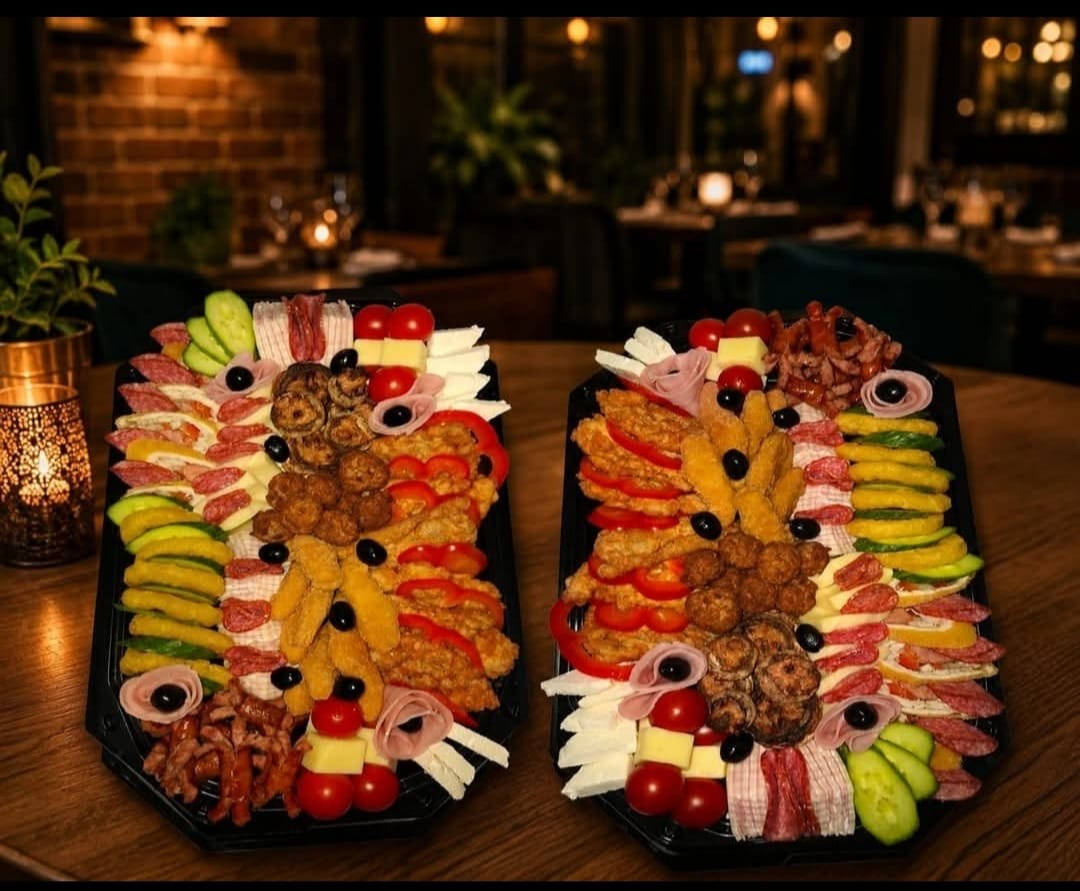 Două platouri de aperitive cu mezeluri, brânzeturi, legume și preparate crocante, pe o masă din restaurant